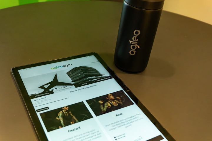 Tablet auf einem runden Tisch, welches den agilea Webvertrag anzeigt, daneben steht eine agilea gebrandete Coffee Mug in schwarz